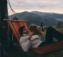 Leave all your worries behind. Handsome young man lying in hammock and reading a book while camping with his girlfriend