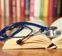 A stethoscope is lying with a book on the desk against books