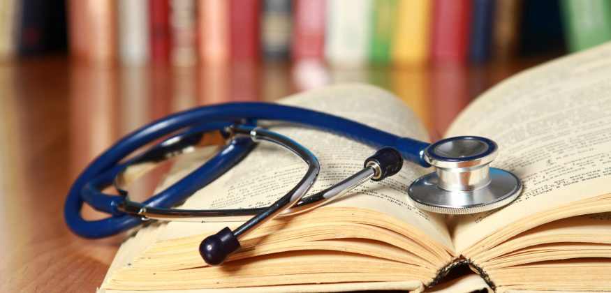 A stethoscope is lying with a book on the desk against books